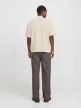 Polo loose de tejido estructurado color beige, con cuello tipo polo, mangas cortas, hombros caídos y cierre frontal con botones.