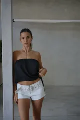 Short de cuero sintético color blanco, de tiro bajo, con cierre frontal y cinturón integrado con tachas metálicas. Presenta cordones laterales ajustables.