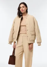 Campera acolchada de color beige con diseño matelasseado, cuello, puños y dobladillo en rib elástico. Cuenta con bolsillos frontales con solapa y cierre de botones a presión.