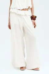 Pantalón oversized de tiro bajo color blanco crudo, confeccionado en viscosa con alforzas, ribetes de encaje, cordón de ajuste y ribete de volado en la cintura.