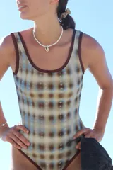 Traje de baño enterizo con estampado abstracto en tonos celeste, beige y marrón, con escote redondo y breteles anchos con vivos en marrón.