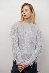 Buzo de punto color beige con cuello redondo, mangas largas con flecos decorativos y diseño de trenzas en el frente.