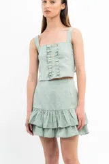 Conjunto de top corto y falda corta color verde agua. El top es de breteles anchos, corte recto y con volados verticales y botones decorativos en el frente. La falda es de corte recto con volados en el ruedo.