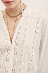 Camisa de manga larga blanca con detalles de encaje y entredos verticales, escote en V y cuello mao con volados sutiles.