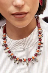 Collar corto compuesto por una alternancia de cuentas de vidrio translúcidas color bordó, cuentas esféricas color naranja y piezas alargadas de piedra natural con estampado tipo dálmata. Incluye cadena de ajuste metálica.