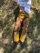 Pantalon de tiro medio y corte recto, confeccionado en tela con textura marcada y acabado rustico. Presenta un estampado artesanal con variaciones de tonos tierra y marrones, evocando un aspecto desgastado y natural.