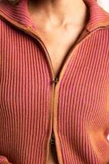 Campera tejida de algodón con diseño acanalado, cuello alto y cierre frontal completo. Presenta un patrón bicolor en tonos terracota y rosado, con puños y cintura elásticos.