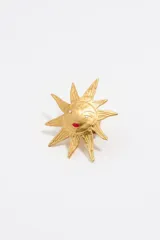 Anillo dorado de metal con forma de sol, rostro con labios rojos y dos incrustaciones brillantes en los ojos.