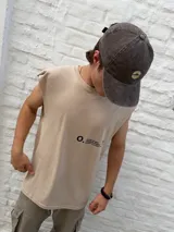 Musculosa de color beige con cuello redondo y corte holgado. Presenta un estampado minimalista en negro en el lateral del pecho con el nombre de la marca Osten Studio y coordenadas geográficas.