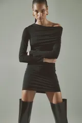 Vestido corto entallado de punto elástico, con diseño asimétrico de un solo hombro y manga larga. Presenta una capa superior drapeada y costuras fruncidas laterales que crean un efecto de pliegues en toda la prenda.