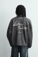 Sudadera de corte relajado confeccionada en tejido de algodón con textura acanalada. Presenta cuello redondo, manga larga y un diseño con efecto lavado. Incluye un texto estampado en contraste en la parte frontal.