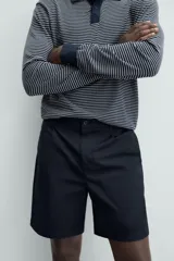 Bermuda de hombre color beige claro, corte regular fit, con pliegues frontales, bolsillos delanteros y bolsillos traseros de doble vivo con botón.