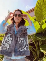 Chaleco reversible con un lado de piel sintética gris y el otro lado de tela bordada con diseño floral y espiral en tonos blanco y negro. Presenta un diseño sin mangas y corte recto.