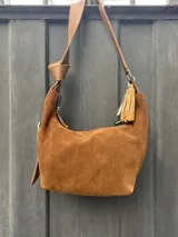 Cartera bandolera de gamuza color marrón topo, con correa ajustable de cuero marrón oscuro.
