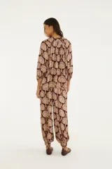 Pantalón babucha de tiro medio en tonos bordó y beige con estampado ornamental. Presenta cintura elastizada con cordón ajustable, diseño amplio y puños elastizados en los tobillos.