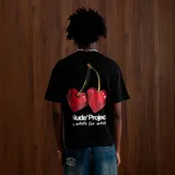 Camiseta negra de corte oversize con estampado de dos cerezas rojas en forma de corazón y el logo de la marca Nude Project en blanco.