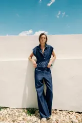 Chaleco de denim azul oscuro con cuello alto, manga sisa y cintura ajustable con elástico. Cierre frontal con botones a presión metálicos.