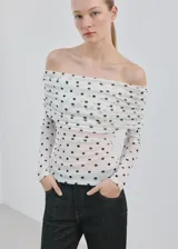 Camiseta blanca de malla con estampado de lunares negros, escote palabra de honor cruzado con fruncidos y manga larga.