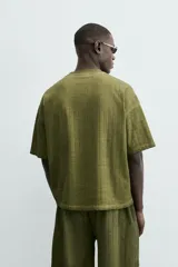 Camiseta de algodón de corte relajado (relaxed fit) con cuello redondo y manga corta. Presenta un tejido acanalado vertical (canalé) y un acabado ligeramente desgastado o lavado en tono verde oliva.