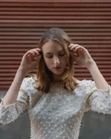 Top corto color crema, de manga media, con espalda baja y cuello bateau confeccionado en tela stretch. Textura de perlas salpicadas aplicadas a mano.