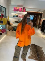 Buzo oversize de plush color naranja, con capucha ajustable por cordones, bolsillo canguro delantero y mangas largas abullonadas con puños elásticos.