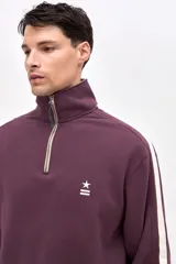 Buzo de felpa con friza, color bordó, con cuello alto y medio cierre metálico frontal. Presenta mangas largas con franjas laterales en color crema y bordado de la marca en el pecho.