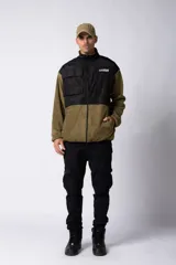 Campera de polar con recortes en tela técnica tipo sire en la parte superior frontal. Presenta cierre frontal completo, cuello alto y bolsillos funcionales en el pecho. Diseño bicolor en tonos verde oliva y negro con logo de la marca en el pecho.