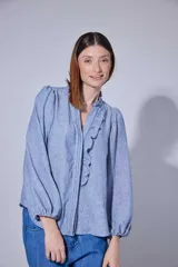 Camisa de lino en tono azul jaspeado, con cuello mao con volados, cierre frontal con botones ocultos y mangas largas abullonadas con puños elásticos.