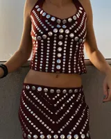 Conjunto de dos piezas compuesto por un top halter y una falda midi, ambos en color bordó con aplicaciones de tachas metálicas circulares plateadas dispuestas en patrones geométricos.