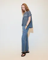 Remera blanca de lino con cuello mao, media cartera con broches metálicos y manga japonesa. Presenta un bolsillo frontal tipo plaqué, recortes laterales en sisa con detalles de encaje y ruedo redondeado con corte escalonado.