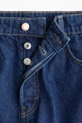 Bermuda de denim azul oscuro, tiro alto, corte ancho, largo a la rodilla y cinco bolsillos. Cierre frontal con botón.