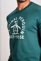 Remera de algodón color verde petróleo con cuello redondo y mangas cortas. Presenta un estampado gráfico frontal en color blanco con el logo de la marca y la leyenda Original Penguin Est. 1955.