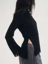 Blusa negra de crepe texturado, con cuello alto, mangas largas acampanadas y corte asimétrico con abertura lateral.