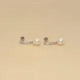 Caravanas colgantes de plata 925, compuestas por una barra horizontal engastada con pequeñas circonias y una perla de río colgante.