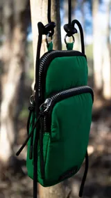 Phone bag de nylon color verde, con compartimento principal y bolsillo frontal con cierre. Incluye correa regulable y desmontable, y cuenta con tarjetero interno y bolsillo trasero.