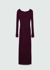 Vestido midi de punto acanalado en color bordó, con cuello barco, manga larga y diseño entallado. Incluye un cinturón desmontable de la misma tela para ajustar a la cintura y presenta una abertura lateral.