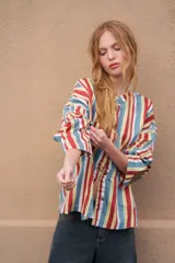 Camisa de denim azul con cuello mao, diseño holgado, mangas largas y cierre frontal con botones metálicos. Cuenta con costuras decorativas pespunteadas en el delantero.