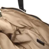 Cartera tipo tote color verde oliva, confeccionada en material sintético con detalles en negro. Cuenta con doble asa superior, correa ajustable extraíble, bolsillos frontales con cierre y logo metálico circular en la parte superior.