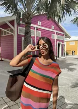 Vestido tejido de algodón con rayas horizontales multicolor (rojo, naranja, rosa, verde, azul, blanco, marrón, negro) y cuello redondo con terminación en crochet azul.