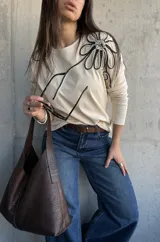 Remera manga larga de color beige, con detalle de aplique floral tridimensional en el hombro confeccionado con cordones en blanco y negro.