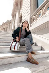 Cartera plateada tipo tote bag con detalles en cuero marrón, doble asa de mano y correa larga ajustable.