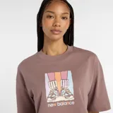Remera corta de manga corta, color marrón topo, con cuello redondo y un estampado frontal que muestra un par de zapatillas New Balance sobre un fondo de bloques de color pastel.