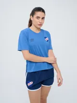 Remera de fútbol Umbro del Club Nacional de Football, modelo Bink para mujer. Diseño azul oscuro con cuello redondo y mangas cortas, con logo de Umbro en el pecho derecho y escudo del club en el pecho izquierdo.