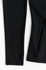 Campera deportiva negra de corte ajustado, con cuello elevado, cierre frontal y bolsillos laterales con cierre. Presenta aberturas para el pulgar en las mangas largas.
