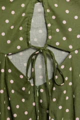 Vestido midi verde militar con estampado de lunares rosados, de corte recto y tirantes finos cruzados en la espalda. Presenta escote con frunces y detalle de lazo en el centro.