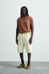 Camiseta tank (sin mangas) de corte relajado, color terracota con efecto lavado y estampado frontal de estrellas en blanco. Presenta cuello redondo y acabados deshilachados en las sisas y el ruedo.