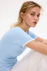 Remera de punto fino color celeste, entallada, de manga corta, con ribetes acanalados blancos en el cuello redondo, puños y dobladillo.