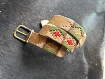 Cinto de cuero marrón claro con detalles bordados geométricos en tonos azul, rojo y beige, hebilla metálica de bronce y puntera forrada en cuero.