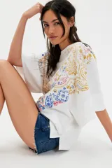 Remera de algodón blanca de corte oversize y silueta recta, con escote redondo, hombros caídos y mangas cortas amplias. Presenta una estampa frontal con diseño paisley en tonos rojo, azul, amarillo y gris.