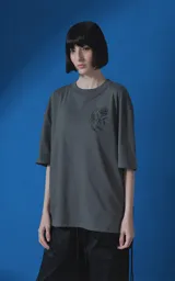 Remera de manga corta con cuello redondo y calce oversize, color gris oscuro. Presenta una estampa frontal con diseño gráfico de un escorpión y una rosa, junto con texto tipográfico.